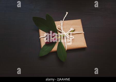 Confezione regalo in confezione artigianale su sfondo nero di legno con fiore di azalea viola Foto Stock