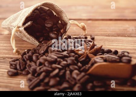 Primo piano dei chicchi di caffè tostati con anice in sacchetto di sacco su sfondo di legno il caffè è sempre una buona idea Foto Stock