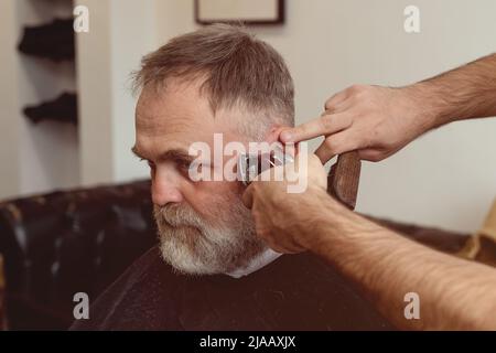 Un uomo anziano che intruda i capelli di un maestro in un barbiere. Un vecchio uomo ottiene un taglio di capelli elegante Foto Stock