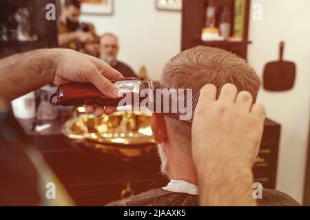 Un uomo anziano che intruda i capelli di un maestro in un barbiere. Un vecchio uomo ottiene un taglio di capelli elegante Foto Stock