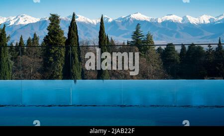 Piscina all'aperto presso il resort. Panorama delle montagne. Neve sulle cime della catena montuosa. Riflesso di alberi e cime di montagna su t Foto Stock