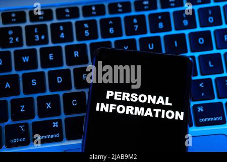 Frase DI INFORMAZIONI PERSONALI visualizzata su uno smartphone posizionato su un notebook sfocato con luce blu dietro di esso. Concetto. Foto Stock