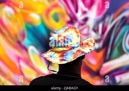 Bristol, Regno Unito. 28th maggio 2022. Un artista di strada che indossa un colorato cappello tinto legato si erge indietro per vedere la sua opera d'arte durante il festival Bristol Upfest Foto Stock