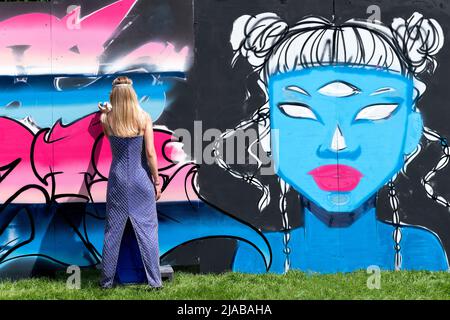 Bristol, Regno Unito. 28th maggio 2022. Una artista di strada femminile, indossando un abito da sera, lavora su un grande murale durante il festival di arte di strada Bristol Upfest Foto Stock