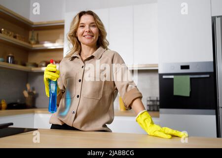 Casalinga adulta in guanti protettivi e con detergente spray bottiglia in cucina Foto Stock