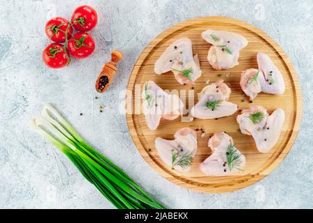 Le ali di pollo crudo si trovano su un supporto rotondo su uno sfondo chiaro con spezie. Foto Stock