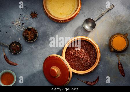 Burro di ghee o chiarificato in ciotole di ceramica e riso rosso con spezie diverse su un vecchio tavolo di legno. Vista dall'alto. Foto Stock