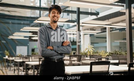 Fiducioso sorridente indiano ragazzo uomo d'affari investitore fondatore direttore di venditore fare incrociate braccia stand in ufficio bello adulto maschio analista Foto Stock