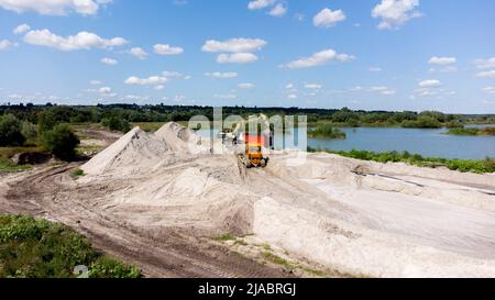 Volo aereo con vista sui droni sulle miniere di sabbia. Cava di sabbia. Vista dall'alto. Lago con acqua blu vicino a pozzo di sabbia. Macchina bulldozer che muove sabbia in cava. Industria mineraria. Attrezzatura mineraria in cava. Foto Stock