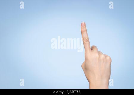 Gesto della mano. La mano femmina mostra il numero uno. Donna che punta verso l'alto con l'indice su sfondo azzurro Foto Stock