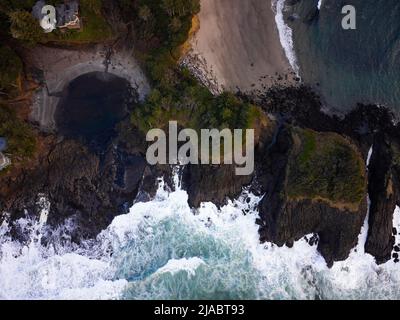 Colpo di drone. Un oceano dalle onde bianche e schiumose, una costa collinare coperta di muschi verdi e pietre sulla riva. La bellezza del selvaggio. Non ci sono peopl Foto Stock