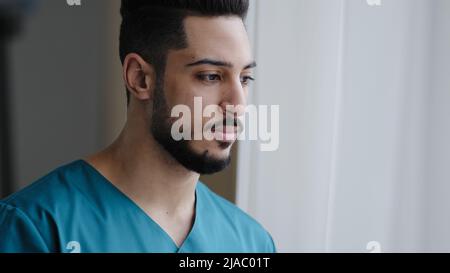 Giovane pene medico ispanico maschio premuroso infermiere arabo terapista chirurgo stare vicino alla finestra in ospedale lavoro attendere paziente Foto Stock