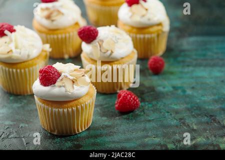 Muffin con panna, lamponi e mandorle su sfondo verde scuro. Cibo dolce, festa, banchetto, compleanno, pic-nic, banchetto. Design del menu. Cu Foto Stock