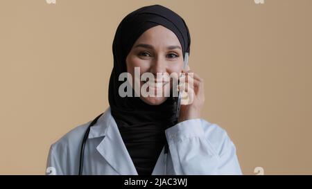 Medico islamico musulmano giovane intern donna araba chirurgo intern in hijab indossare camice medico parlare con cellulare con paziente consulente femminile consultare lontano Foto Stock