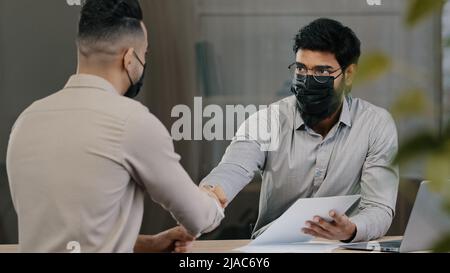 Avvocato arabo banchiere uomo d'affari ispanico uomo di vendita analista in maschera medica consultare cliente malato discutere di assicurare contratto scuotendo le mani Foto Stock
