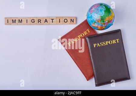 Composizione piatta con passaporti, globo e iscrizione immigrazione scritta su cubi di legno. Spazio per il testo. Foto Stock