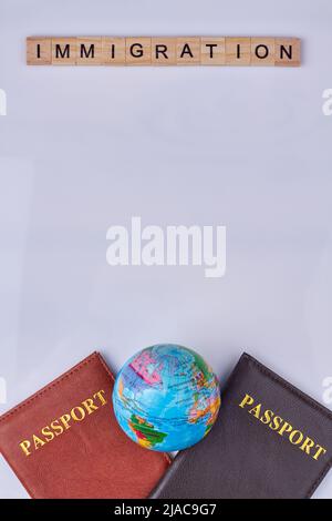 Iscrizione immigrazione su cubi di legno. Due passaporti e globo. Composizione con disposizione piatta con spazio di copia. Foto Stock
