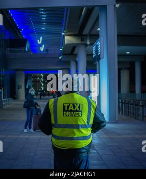 Ritratto posteriore di un tassista in piedi al terminal 2, aeroporto di Manchester, in attesa di clienti. Foto Stock