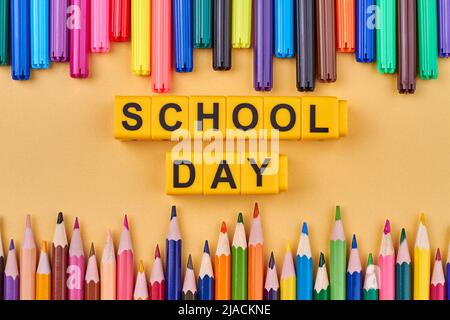 La giornata scolastica dell'iscrizione scritta a cubetti gialli. Colorati rifornimenti scolastici sul tavolo. Disposizione piatta. Foto Stock