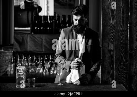 Bel barman con bearded e barba lunga e baffi con serio cocktail alcolico fatto sul viso in pelle scamosciata vintage su sfondo viola rosso bar. Foto Stock