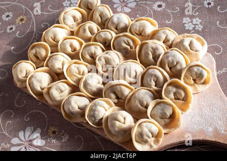 Gnocchi Siberiani fatti in casa con ripieno di carne su un tagliere di legno, sul tavolo. Preparazione di un delizioso piatto russo ad alto contenuto calorico. Foto Stock