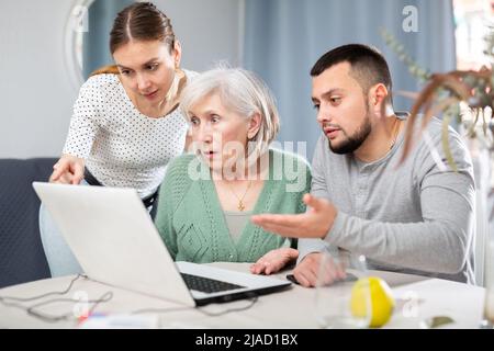Coppia giovane che aiuta la donna anziana ad usare il laptop Foto Stock