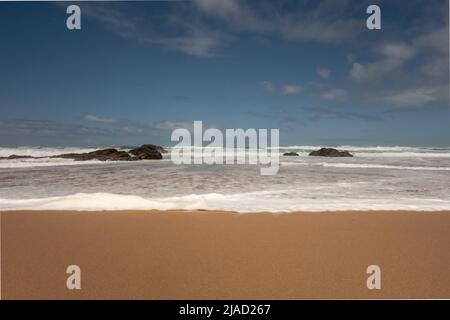 Onde che si rotolano verso la spiaggia di Guincho - Praia do Guincho - a bassa marea mentre si infrangono sopra le rocce costiere partito sommerso in Cascais Portogallo Foto Stock