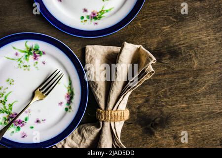 Stoviglie floreali vintage su un tavolo di legno con un tovagliolo rustico Foto Stock