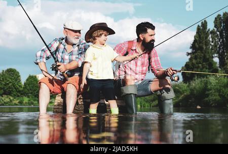 Uomo che insegna ai bambini come pescare nel fiume. Nonno, padre e ragazzo che pescano insieme. Papà e figlio pesca al lago. Fine settimana estivo. Foto Stock