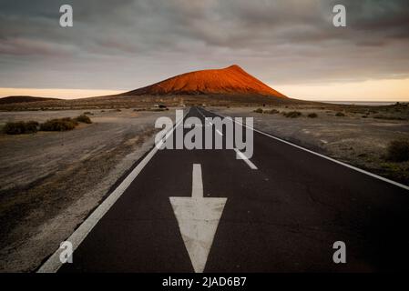 Strada dritta che porta alla montagna rossa (Montana Roja) al tramonto, El Medano, Tenerife, Isole Canarie, Spagna Foto Stock