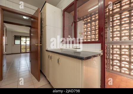 Mobili da cucina color crema e piano di lavoro in legno con accesso ad una terrazza asciugante con porte in alluminio e vetro con traliccio in calcestruzzo Foto Stock