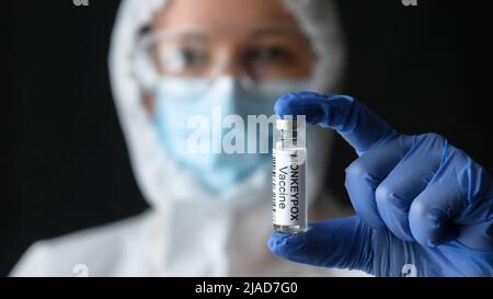 Monkeypox vaccino in mano medici, medico femminile in dispositivi di protezione personale (PPE) mostra bottiglia per shot dal vaiolo. Concetto di scimmia Foto Stock
