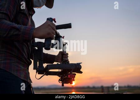 Uomo che usa un gimbal e stabilizzatore per girare un video al tramonto Foto Stock