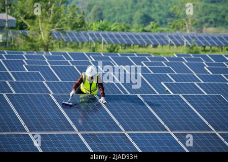 Ingegnere pulizia pannelli solari in una stazione a energia solare, Thailandia Foto Stock