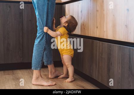 Ritratto di ragazza emotiva bambino tenendo le gambe della madre in piedi in cucina. Bellissimo ritratto. Concetto di infanzia. Foto Stock