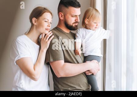 Felice multinazionale padre giovane uomo e madre con bambina figlia piccola divertirsi vicino alla finestra di casa Foto Stock