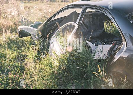 Discarica di auto, rottami di metallo. Primo piano di una vecchia auto abbandonata in un cortile con erba che germogliano all'interno e ciottoli troppo coltivati. Il sole si riflette Foto Stock