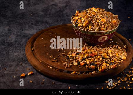Una miscela di semi di grano, mais e girasole versata in una ciotola di ceramica su un asse di legno Foto Stock