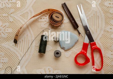 Su un tessuto di lacy sono disposti uno strappo di cucitura, gesso del sarto, ago e filo, spilli di bobina e altro attrezzo che i dressmakers e sarti funzionano con. Foto Stock