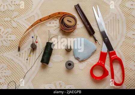 Su un tessuto di lacy sono disposti uno strappo di cucitura, gesso del sarto, ago e filo, spilli di bobina e altro attrezzo che i dressmakers e sarti funzionano con. Foto Stock