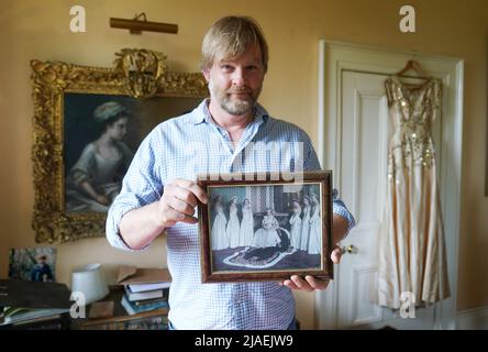 Rory Campbell, nella sua casa a Randalstown, Co. Antrim, tenendo una fotografia di sua madre Lady Moyra Campbell (a sinistra) con la regina Elisabetta II il giorno dell'incoronazione, insieme al vestito Lady Campbell indossava come una cameriera d'onore all'incoronazione della regina nel 1952. L'abito sarà esposto come parte di una speciale mostra giubilare di diamanti al Castello di Enniskillen. Data immagine: Giovedì 26 maggio 2022. Foto Stock