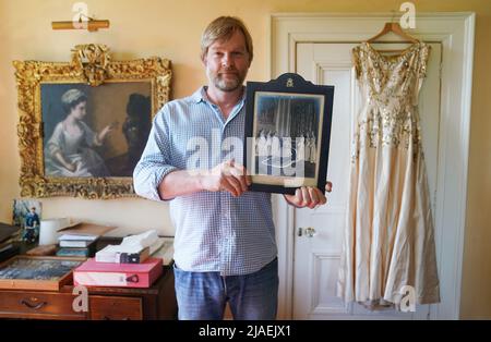 Rory Campbell, nella sua casa a Randalstown, Co. Antrim, tenendo una fotografia di sua madre Lady Moyra Campbell (a sinistra) con la regina Elisabetta II il giorno dell'incoronazione, insieme al vestito Lady Campbell indossava come una cameriera d'onore all'incoronazione della regina nel 1952. L'abito sarà esposto come parte di una speciale mostra giubilare di diamanti al Castello di Enniskillen. Data immagine: Giovedì 26 maggio 2022. Foto Stock