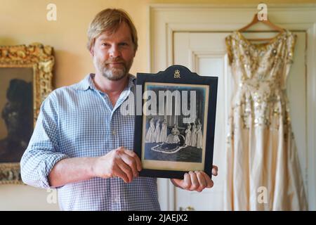 Rory Campbell, nella sua casa a Randalstown, Co. Antrim, tenendo una fotografia di sua madre Lady Moyra Campbell (a sinistra) con la regina Elisabetta II il giorno dell'incoronazione, insieme al vestito Lady Campbell indossava come una cameriera d'onore all'incoronazione della regina nel 1952. L'abito sarà esposto come parte di una speciale mostra giubilare di diamanti al Castello di Enniskillen. Data immagine: Giovedì 26 maggio 2022. Foto Stock