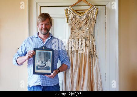 Rory Campbell, nella sua casa a Randalstown, Co. Antrim, tenendo una fotografia di sua madre Lady Moyra Campbell (a sinistra) con la regina Elisabetta II il giorno dell'incoronazione, insieme al vestito Lady Campbell indossava come una cameriera d'onore all'incoronazione della regina nel 1952. L'abito sarà esposto come parte di una speciale mostra giubilare di diamanti al Castello di Enniskillen. Data immagine: Giovedì 26 maggio 2022. Foto Stock