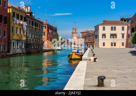 Strada lungo il canale e vecchie case colorate come la torre dell'Arsenale veneziano sullo sfondo a Venezia, Italia. Foto Stock