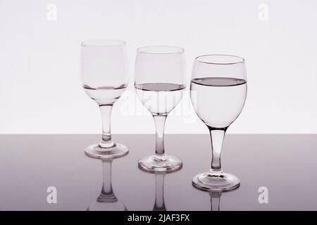 Tre bicchieri di vino riempiti di acqua riflessa sul tavolo Foto Stock
