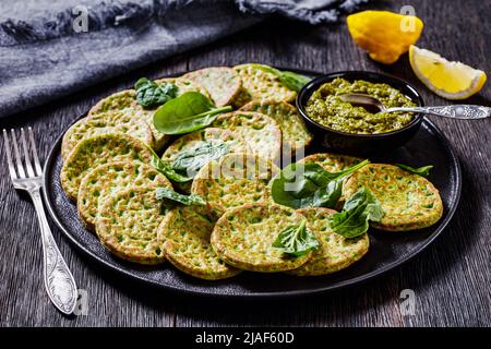 pancake di spinaci sani su piatto nero con pesto di basilico su tavola di legno scuro, vista orizzontale dall'alto Foto Stock