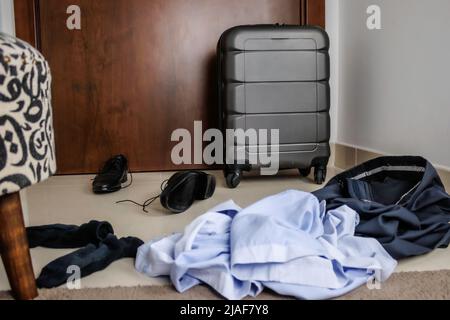 vista posteriore di un uomo d'affari irriconoscibile che sta per lasciare la casa con una valigia, egli porta una valigia su ruote Foto Stock