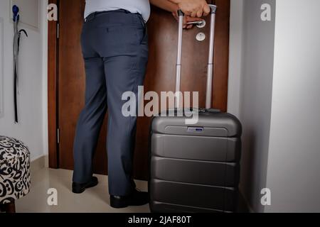 vista posteriore di un uomo d'affari irriconoscibile che sta per lasciare la casa con una valigia, egli porta una valigia su ruote Foto Stock