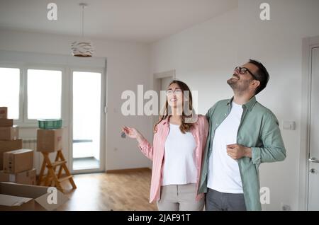 Giovane coppia sorridente guarda intorno al loro nuovo appartamento e sembrano soddisfatti mentre la donna tiene le chiavi in mano Foto Stock